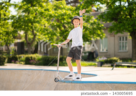 Boy in a hat with a scooter in a skatepark looking contented 143005695