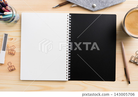 Top view of open spiral notebook mockup with black and white pages on light wooden desk 143005706