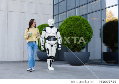 Young woman holding paper cup gesturing while walking with robot Young woman holding paper cup gesturing while walking with robot 143005735
