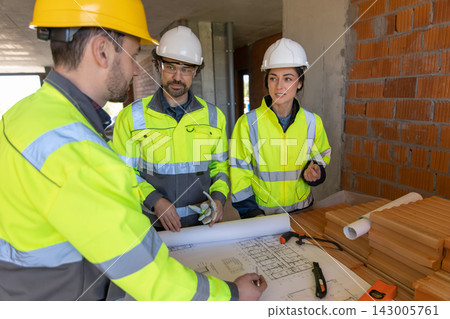 Construction team examining blueprints on table Construction team examining blueprints on table 143005761
