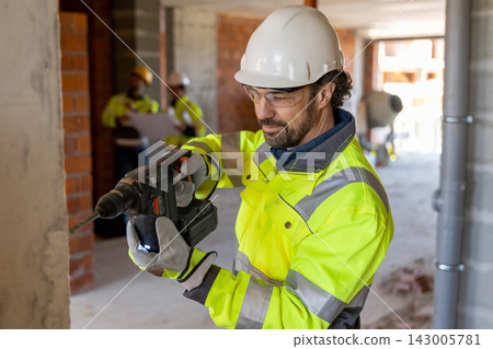 Focused builder using hammer drill on wall Focused builder using hammer drill on wall 143005781