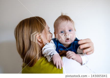 Happy young mother holding her cute baby boy on a light background with copy space. Happy young mother holding her cute baby boy on a light background with copy space. 143005841