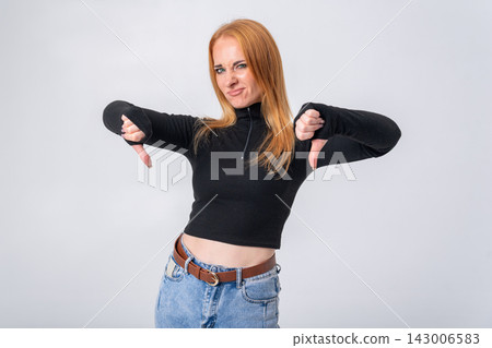 Young woman expressing disapproval or rejection by holding both hands in a thumbs down gesture, representing negative feedback, dissatisfaction, and disagreement on a clean background Young woman expressing disapproval or rejection by holding both hands in a thumbs down gesture, representing negative feedback, dissatisfaction, and disagreement on a clean background 143006583