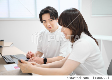 一位年輕女子和她的男同事正在使用平板電腦。 一位年輕女子和她的男同事正在使用平板電腦。 143007221