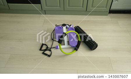 Mini stepper machine with pilates ring and foam roller on floor at home. Domestic fitness equipment set. Compact workout gear for indoor cardio and strength training. Home gym and weight loss concept. Mini stepper machine with pilates ring and foam roller on floor at home. Domestic fitness equipment set. Compact workout gear for indoor cardio and strength training. Home gym and weight loss concept. 143007607