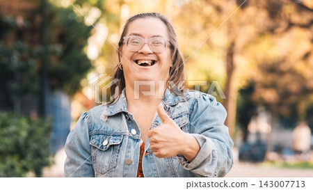 Happy woman with down syndrome showing thumbs up in a park Happy woman with down syndrome showing thumbs up in a park 143007713