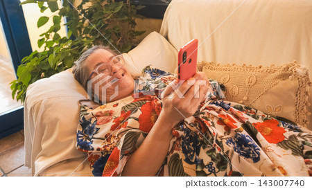 Happy woman with down syndrome relaxing on sofa using smartphone Happy woman with down syndrome relaxing on sofa using smartphone 143007740