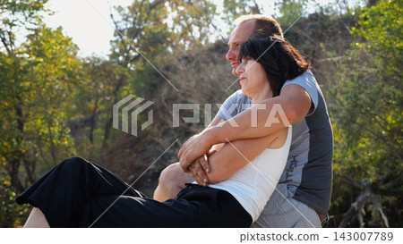 Happy pair hugs during sitting on wooden log on beach. Romantic couple admiring sea landscape at sunny day. Lovers spending time together at resort. Concept of summer vacation or holiday. Slow mo Happy pair hugs during sitting on wooden log on beach. Romantic couple admiring sea landscape at sunny day. Lovers spending time together at resort. Concept of summer vacation or holiday. Slow mo 143007789
