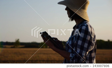 Female agronomist in straw hat monitoring harvest on barley field at sunset. Adult farmer using digital tablet on wheat meadow at dusk. Beautiful scenic landscape. Concept of agricultural business Female agronomist in straw hat monitoring harvest on barley field at sunset. Adult farmer using digital tablet on wheat meadow at dusk. Beautiful scenic landscape. Concept of agricultural business 143007806