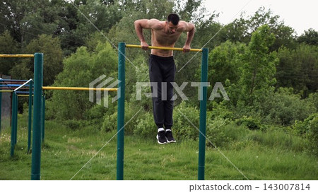 Hardy shirtless sportsman doing push ups on horizontal bar at nature. Strong and muscular guy training at sports ground. Young athletic guy exercising outdoor. Concept of active and healthy lifestyle Hardy shirtless sportsman doing push ups on horizontal bar at nature. Strong and muscular guy training at sports ground. Young athletic guy exercising outdoor. Concept of active and healthy lifestyle 143007814