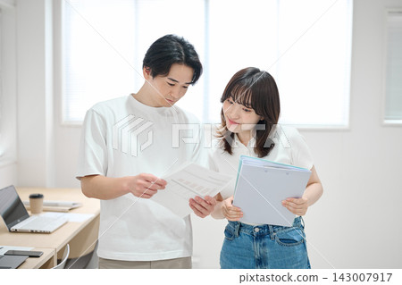 一對年輕男女正在辦公室查看文件。 一對年輕男女正在辦公室查看文件。 143007917