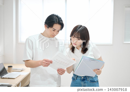 一對年輕男女正在辦公室查看文件。 143007918