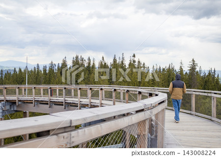 Man walking on panoramic wooden platform with dramatic mountain landscape in High Tatras near Zakopane. Solo travel, outdoor exploration and scenic tourism lifestyle concept. Man walking on panoramic wooden platform with dramatic mountain landscape in High Tatras near Zakopane. Solo travel, outdoor exploration and scenic tourism lifestyle concept. 143008224