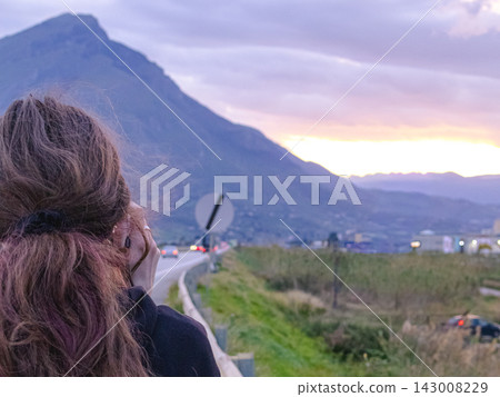 Close view of female traveler looking at sunset road landscape in Sicily near Palermo. Emotional travel moment, Mediterranean freedom, scenic journey and vacation inspiration concept. Close view of female traveler looking at sunset road landscape in Sicily near Palermo. Emotional travel moment, Mediterranean freedom, scenic journey and vacation inspiration concept. 143008229