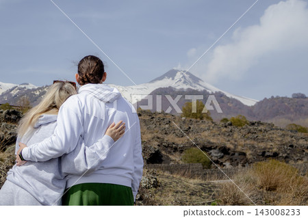 Couple standing and embracing while looking at Mount Etna volcano landscape. Travel, relationship and shared moments concept, enjoying scenic view in early spring nature. Couple standing and embracing while looking at Mount Etna volcano landscape. Travel, relationship and shared moments concept, enjoying scenic view in early spring nature. 143008233