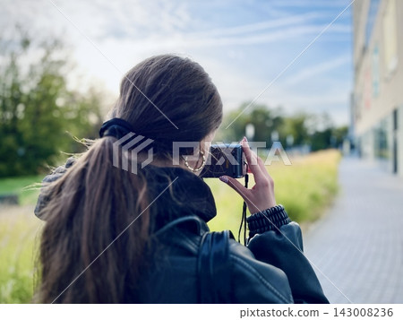 Rear view of teenage girl holding and shooting with vintage camera in urban park. Embracing slow photography, digital detox, and creative nostalgia. Authentic youth lifestyle Rear view of teenage girl holding and shooting with vintage camera in urban park. Embracing slow photography, digital detox, and creative nostalgia. Authentic youth lifestyle 143008236