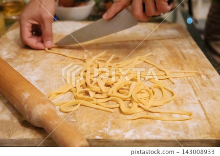 Hand cutting fresh dough into noodles with kitchen knife 143008933