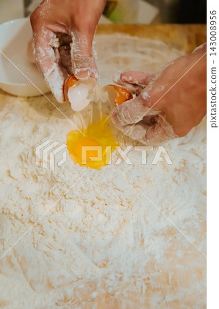 Adding raw egg into flour for making pasta dough Adding raw egg into flour for making pasta dough 143008956