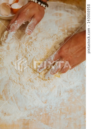 Hands mixing egg and flour into pasta dough top view Hands mixing egg and flour into pasta dough top view 143008958