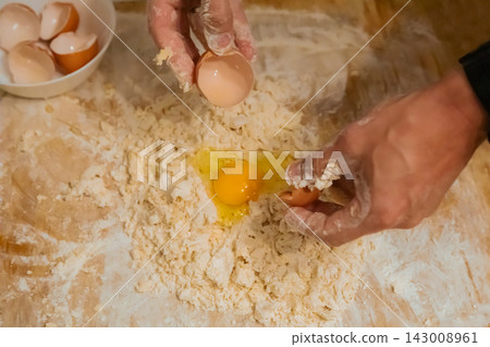 Hands kneading dough with egg yolk on wooden table Hands kneading dough with egg yolk on wooden table 143008961