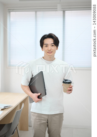 一位身著商務休閒裝的年輕男子,手提一台筆記型電腦。 一位身著商務休閒裝的年輕男子,手提一台筆記型電腦。 143009088
