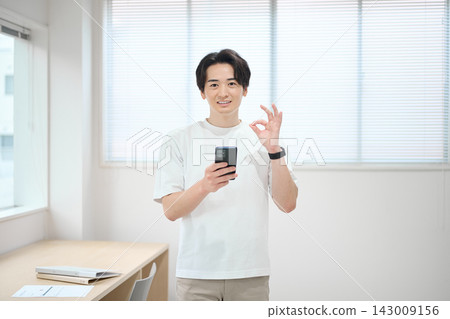 一位身著休閒職業裝的年輕男子手持智慧型手機 一位身著休閒職業裝的年輕男子手持智慧型手機 143009156