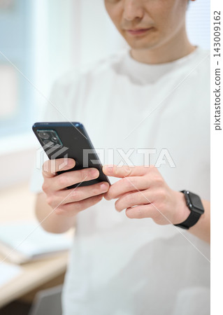 一位身著休閒職業裝的年輕男子手持智慧型手機 一位身著休閒職業裝的年輕男子手持智慧型手機 143009162