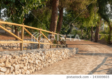 Wooden fence on top of a stone gabion wall along a dirt path in a park Wooden fence on top of a stone gabion wall along a dirt path in a park 143009603