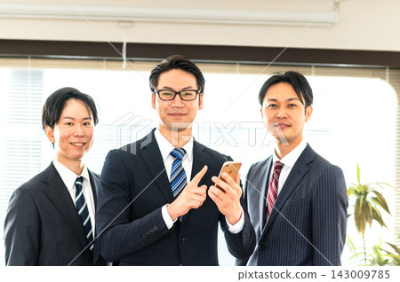 三名身穿西裝的男子和一名身穿西裝、手持智慧型手機的男子正在指向。 143009785