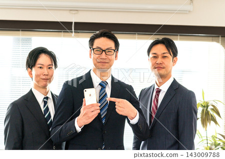 三名身穿西裝的男子和一名身穿西裝、手持智慧型手機的男子正在指向。 143009788