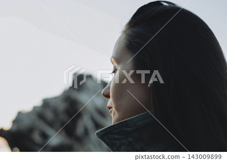 Pensive woman standing by the sea in soft natural light, viewed in close profile with long dark hair, creating a quiet atmospheric portrait about solitude, reflection, emotional travel and inner calm. Pensive woman standing by the sea in soft natural light, viewed in close profile with long dark hair, creating a quiet atmospheric portrait about solitude, reflection, emotional travel and inner calm. 143009899