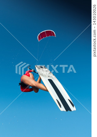 Woman Kitesurfer jumping high in the air against blue sky Woman Kitesurfer jumping high in the air against blue sky 143010026