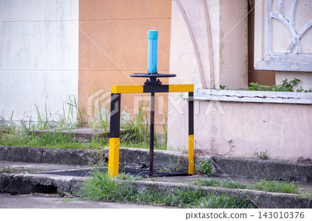 Yellow and black safety-painted manual sluice gate water control valve mounted on concrete drainage cover in urban infrastructure 143010376