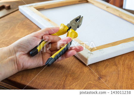 Artist Holding Pliers Above Canvas Stretcher Frame on Wooden Table. Art Framing and Stretching Concept Artist Holding Pliers Above Canvas Stretcher Frame on Wooden Table. Art Framing and Stretching Concept 143011238