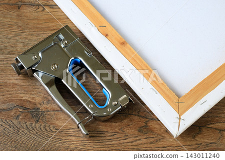 Hand Tacker Staple Gun Beside Stretcher Frame Corner on Wooden Table. Art Framing Concept Hand Tacker Staple Gun Beside Stretcher Frame Corner on Wooden Table. Art Framing Concept 143011240