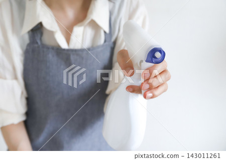 一位繫著圍裙的家庭主婦正在噴灑某些東西。 一位繫著圍裙的家庭主婦正在噴灑某些東西。 143011261