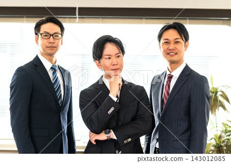 三個穿西裝的男人，還有一個穿西裝的男人正在用智慧型手機通話。 143012085