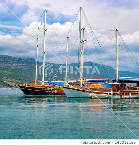 Traditional wooden gulet yachts anchored on calm turquoise sea against scenic coastal mountains, square orientation shot featuring sky and water copy space for vacation concepts. Traditional wooden gulet yachts anchored on calm turquoise sea against scenic coastal mountains, square orientation shot featuring sky and water copy space for vacation concepts. 143012186