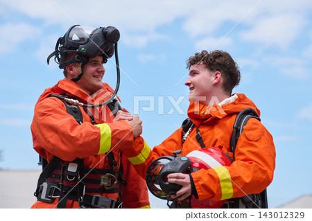 Two Firefighters in Orange Protective Gear Celebrating Teamwork After Rescue Training Exercise Two Firefighters in Orange Protective Gear Celebrating Teamwork After Rescue Training Exercise 143012329