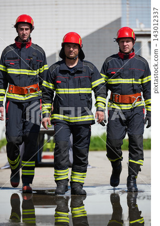 Three Firefighters Walking Confidently In Protective Gear With Red Helmets And Reflective Stripes Three Firefighters Walking Confidently In Protective Gear With Red Helmets And Reflective Stripes 143012337