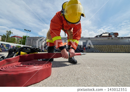 Firefighter Preparing a Fire Hose During Outdoor Training Drill Wearing Protective Gear 143012351