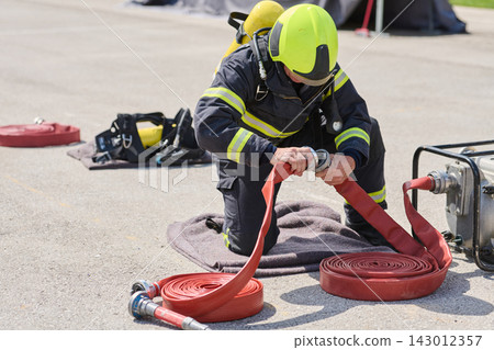 Firefighter Connecting Red Fire Hose During Training Drill With Protective Gear And Helmet Firefighter Connecting Red Fire Hose During Training Drill With Protective Gear And Helmet 143012357