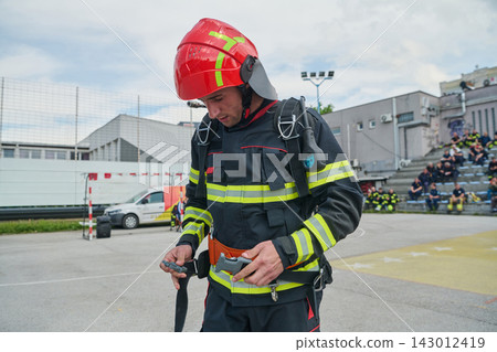 Firefighter Preparing Safety Harness in Red Helmet During Training Exercise at Outdoor Station 143012419