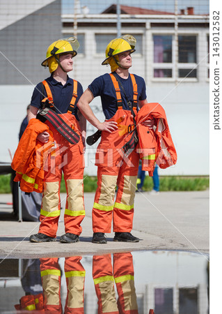 Two Firefighters in Orange Turnout Gear Standing Confidently With Helmets and Jackets Two Firefighters in Orange Turnout Gear Standing Confidently With Helmets and Jackets 143012582