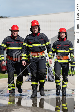 Firefighters Walking In Uniform With Red Helmets Responding As A Team During Emergency Training Exercise Firefighters Walking In Uniform With Red Helmets Responding As A Team During Emergency Training Exercise 143012586