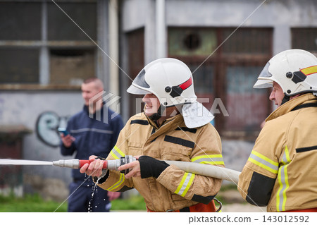 Firefighters Training With Hose During Urban Fire Drill Wearing Protective Helmets And Gear Firefighters Training With Hose During Urban Fire Drill Wearing Protective Helmets And Gear 143012592