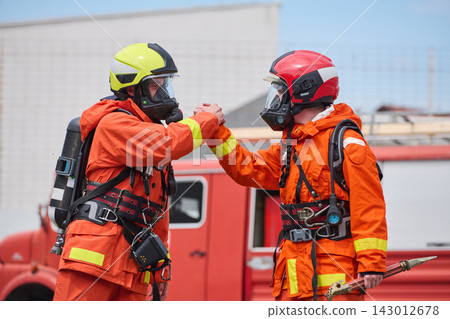 Firefighters Fist Bump in Full Protective Gear During Emergency Response With Fire Truck in Background 143012678