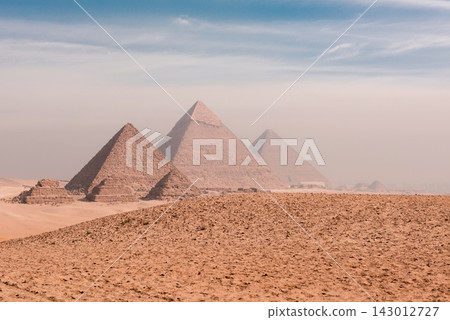 Awe inspiring panoramic view of the ancient Giza pyramids rising from the sandy Egyptian desert plateau under a soft hazy sky perfect for travel Awe inspiring panoramic view of the ancient Giza pyramids rising from the sandy Egyptian desert plateau under a soft hazy sky perfect for travel 143012727
