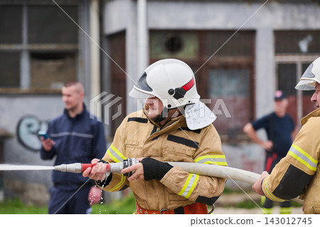 Firefighters Wearing Helmets Operating Fire Hose During Outdoor Training Exercise At Urban Station Firefighters Wearing Helmets Operating Fire Hose During Outdoor Training Exercise At Urban Station 143012745