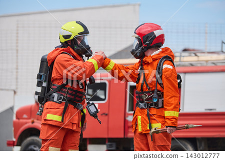 Firefighters Teamwork and Camaraderie in Protective Gear With Breathing Apparatus by Fire Truck Firefighters Teamwork and Camaraderie in Protective Gear With Breathing Apparatus by Fire Truck 143012777